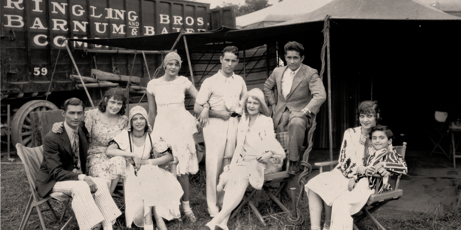 The Colleano Heart A group of circus performers seated in front of tents and metal containers that have Ringling Bros printed on them.